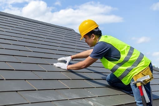 Construction worker standing on a roof covering it with tiles in Owings Mills and Reisterstown, MD